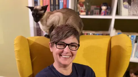 LOUISE SOLOMON Louise Solomon sitting at home with a cat on her chair