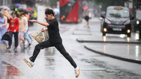 Leon Neal/Getty Images Man jumping over a puddle in London while crossing a road