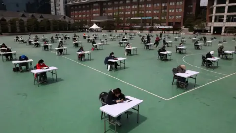 Getty Images South Korean students wear masks and sit according to social distancing for an insurance planner examination at a playground in a Seoul university in April 2020