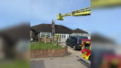 London Fire Brigade Image showing firefighters use an extending ladder to reach the chimney of the bungalow