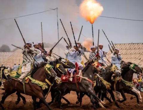 AFP Horsemen riding with rifles in the air. One of the rifles is shooting out fire.