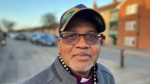 Sam Read/BBC Man with glasses wearing a cap and standing outside