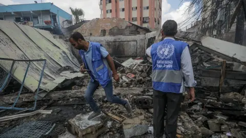EPA Unrwa staff inspect a destroyed building next to a UN-run school filled with displaced people in Nuseirat refugee camp, in central Gaza (14 May 2024)