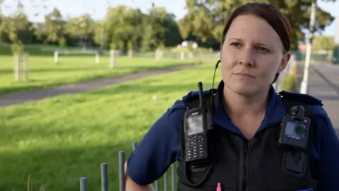 Female police officer in uniform stands next to a grassy area