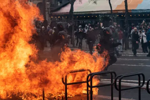 Samuel Boivin/NurPhoto/REX/Shutterstock BRAV-M (Brigade de Repression de l'Action Violente - Mobile) riot police officers run behind a burning barricade on March 23, 2023 in Paris