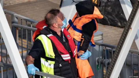 Getty Images A Border Force official carries a young migrant to safety