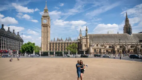 PA Media A couple pose for a selfie on the dried-up grass in Parliament Square, in Westminster, London