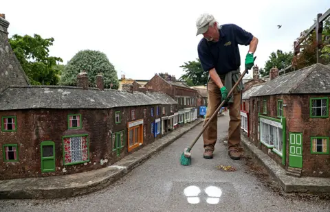 Andrew Matthews/PA Media A man sweeps the ground in the middle of a street in a model town