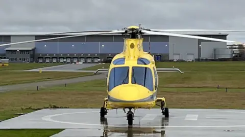 Ollie Conopo/BBC Yellow helicopter standing on the tarmac at a small airport