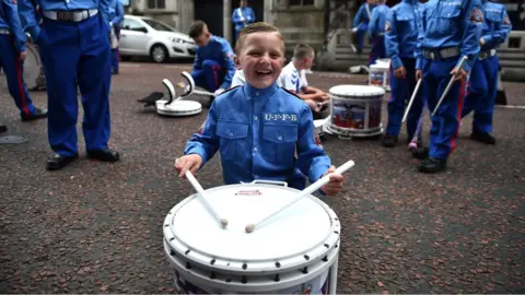 Getty Images A young boy in a band uniform smiles as he plays a drum