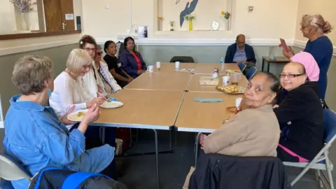 James Grant/BBC A group of eight people. some with drinks, sit around a table