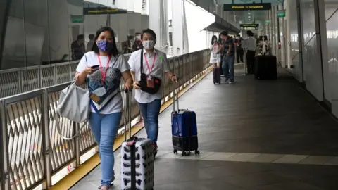 Getty Images Passengers walk toward the World Dream cruise ship docked at Marina Bay Cruise Centre before its departure to "cruises to nowhere" in Singapore on November 6, 2020 in a bid to revive its pandemic-hit tourism industry.