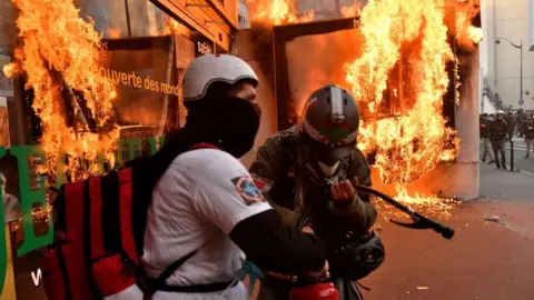 Getty Images Firefighters try to extinguish the flames after protesters burn a billboard during a protest against the government's pension overhaul in Paris, France, January 11, 2020