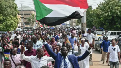 Getty Images A man flashes the victory gesture while waving a Sudanese national flag during a mass demonstration