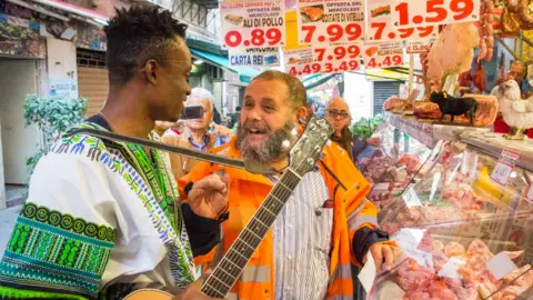 Helen Hecker Singer Chris Obehi being created by Sicilians at a butcher's shop in Sicily