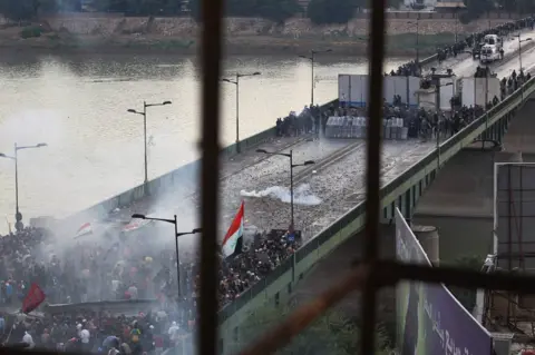 AFP Iraqi security forces fire tear gas to stop protesters attempting to cross al-Jumhuriya bridge from Tahrir Square, Baghdad (25 October 2019)