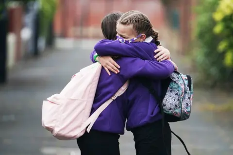 Owen Humphreys / PA Media Two grils wearing masks embrace each other