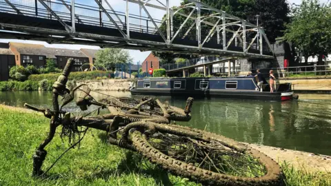 Esther Johnson Long boat going under Grandpont Bridge by a dredged up bike