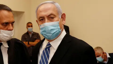 Reuters Israeli Prime Minister Benjamin Netanyahu, wearing a mask, stands inside the courtroom as his corruption trial opens on 24 May 2020