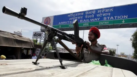 EPA A Punjab policeman stands guard with a gun outside the railway station as trains are cancelled in Amritsar, India, on 26 August 2017.