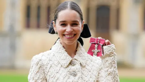 Reuters Emilia Clarke smiles while holding her MBE