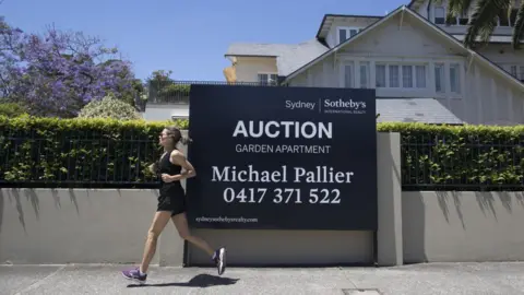Getty Images A woman runs past an auction sign in Sydney