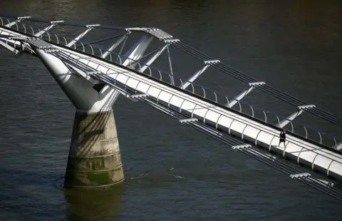 HANNAH MCKAY / Reuters A woman walks across an empty Millennium Bridge during rush hour