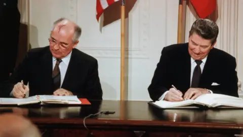 Getty Images Reagan and Gorbachev Signing Arms Limitation Agreement at a table in front of their nations' flags.