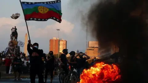 Getty Images A protester waves a Mapuche flag while walking near a fire during a protest against President Sebastian Piñera on March 5, 2021 in Santiago, Chile.