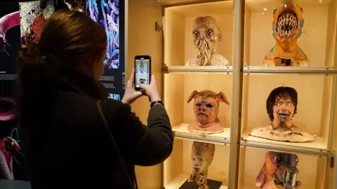 PA Media A visitor takes photos of masks from Doctor Who