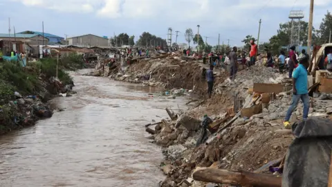 Peter Njoroge/BBC River running through slum area with demolished houses nearby