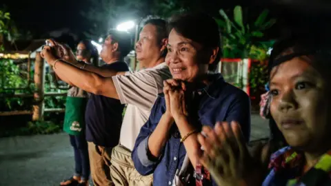 Getty Images An onlooker clasps her hands as she cheers on ambulance taking the children