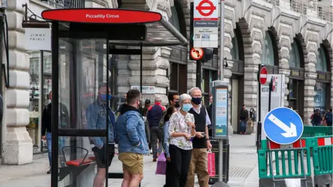 Getty Images people wearing masks waiting a bus stop