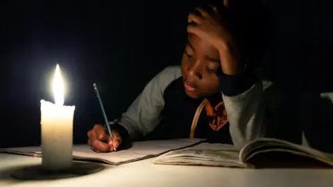 AFP A child doing his homework by candlelight in Harare, Zimbabwe - June 2019