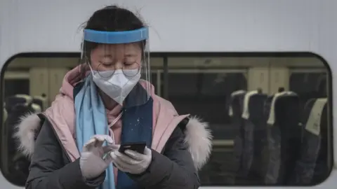 Getty Images A masked traveller sends a message on her phone on the platform at Hankou Railway Station in Wuhan