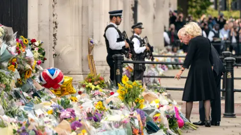PA Media King Charles and Queen Camilla look at flowers outside Buckingham Palace