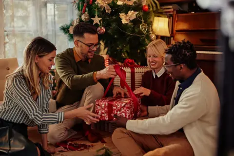 bernardbodo/Getty Cheerful friends opening Christmas present together