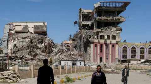 Reuters People walk past destroyed University of Mosul buildings (11 July 2017)