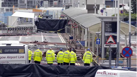 Getty Images Police officers search the area where a burning car slammed into a terminal at Glasgow airport a day after the attack