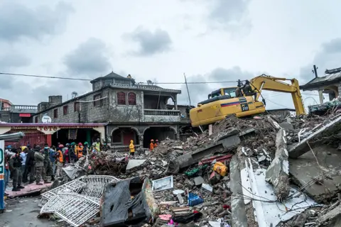 AFP A bulldozer clears the rubble of a building that collapsed in the earthquake in Brefet, a neighborhood of Les Cayes, Haiti, on 17 August 2021
