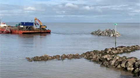 Somerset West And Taunton Council    A digger placing rocks in the sea close to the Somerset coast at Watchet