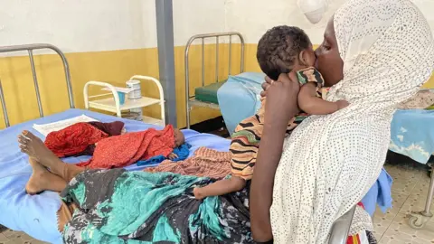 BBC/ Ed Habershon Hawa holding her two-mon-old daughter Ubah and Abdiwali lying on the bed, the day before he died