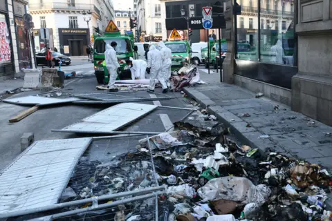 YVES HERMAN/reuters Employees clean up burnt garbage and damage in a street the day after clashes during protests over French government's pension reform in Paris, France, March 24, 2023.