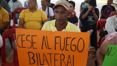 A man holds a sign calling for a ceasefire during a dialogue table between the Colombian government and FARC dissidents in Suarez, Colombia, 19 September 2023.