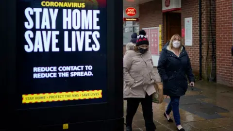 Getty Images Two women walk past a stay home sign in Hyde, Greater Manchester