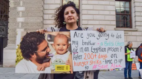 Getty Images Sanaa Seif holds a picture of her brother and a placard asking if the UK Government will let her brother die in prison, during the demonstration outside the Foreign, Commonwealth and Development Office.