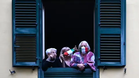 AFP People with protective masks look from their windows at artists performing in the courtyard of a popular apartment building in Rome