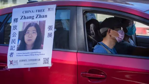 Getty Images A car follows a funeral caravan with poster of Zhang Zhan, a Chinese citizen journalist who criticized the Chinese government's handling of the coronavirus crisis and is being held in a Shanghai prison.