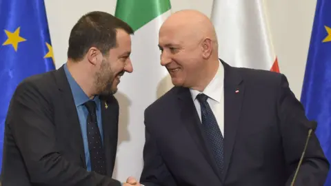 Getty Images Matteo Salvini, left, smiles and shakes hands with Joachim Brudzinski at a press conference event - behind the pair are both nation's flags and the flag of the EU