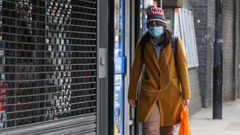 Getty Images A woman wears a face covering while walking down a street in London